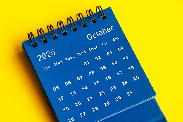 October 2025 blue desk calendar on yellow cover background