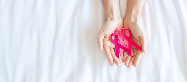 Ottobre mese della consapevolezza del cancro al seno, mano di donna adulta che tiene il nastro rosa su sfondo rosa per sostenere le persone che vivono e le malattie. concetto di giornata internazionale delle donne, della madre e del cancro del mondo