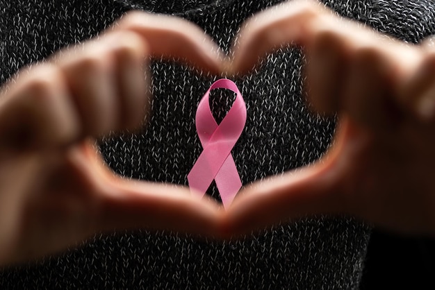 October Breast Cancer Awareness Month, an adult woman wearing a dark T-shirt with a pink ribbon in her hand to support people living and sick. International woman, mother and world cancer day concept.