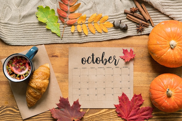 Foto calendario di ottobre tra pasticceria fresca con tè, zucche mature, foglie e spezie sulla tavola di legno