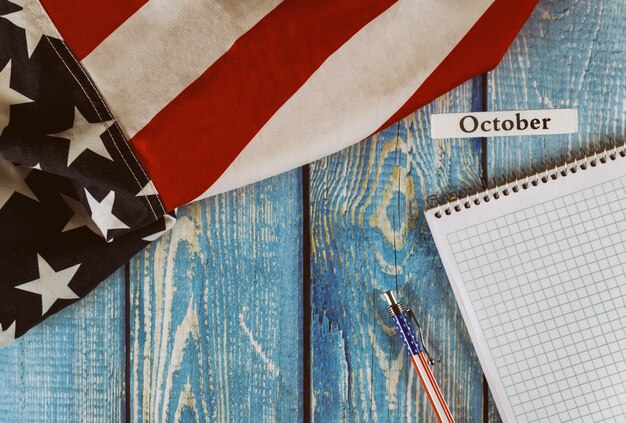 Photo october month of calendar year united states of america flag of symbol of freedom and democracy with blank notepad and pen on office wooden table