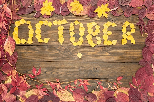 October month name made from yellow leaves on wooden background with colorful autumn leaves frame