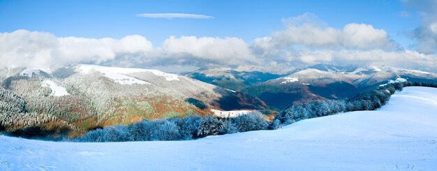 October mountain beech forest edge with first winter snow and last autumn colourful foliage on far mountainside. Two shots stitch image.