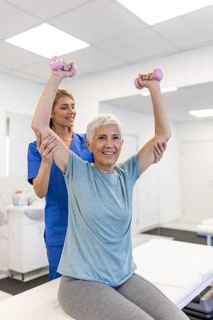 Foto donna anziana che fa fisioterapia con il supporto di fisioterapisti donna anziana anziana seduta in clinica usando manubri esercizio di allenamento per paziente con caregiver in assistenza infermieristica