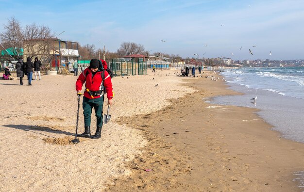 Odessa Oekraïne 07022022 Een man zoekt naar kostbaarheden met behulp van metaaldetector op het strand van Luzanivka in Odessa, Oekraïne op een zonnige winterdag