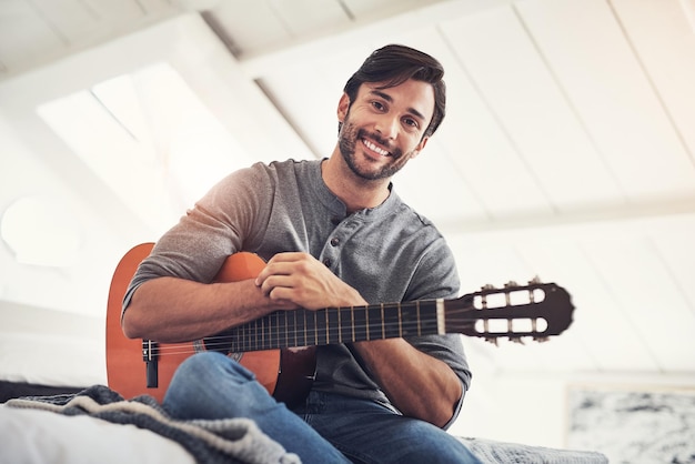 Oefening baart kunst Shot van een knappe jongeman die thuis gitaar oefent