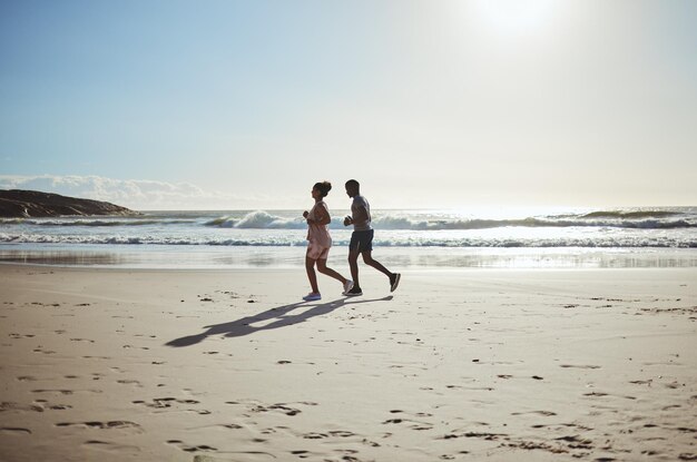 Oefening paar en strand rennen bij zonsopgang voor gezondheidstraining en wellness in de natuur tegen blauwe hemelachtergrond fitness familie en vrouw met man op zand rennen langs de zee training en cardio