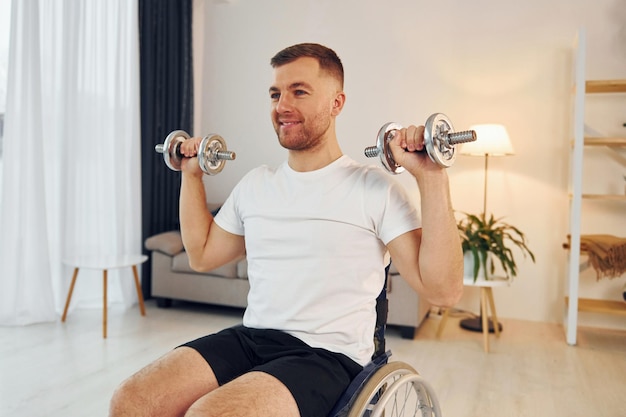 Oefeningen doen met dumbbells gehandicapte man in rolstoel is thuis