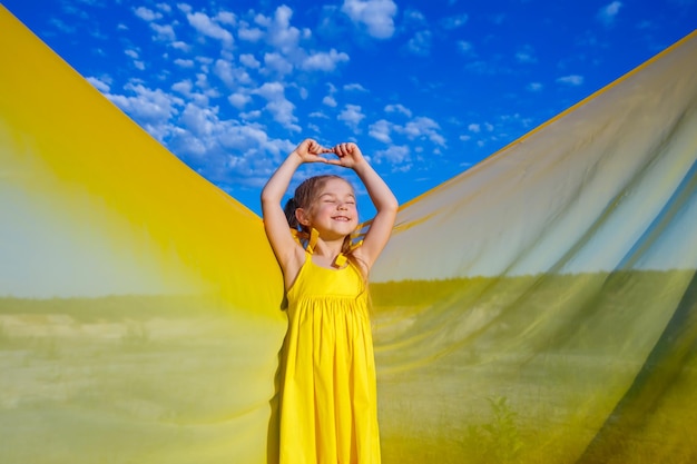 Oekraïens meisje van 7 jaar oud, ze is een patriot van Oekraïne, gekleed in een gele jurk tegen een blauwe lucht Blauwe lucht Zonnige dag Gratis Oekraïens kind Kindsymbool van Oekraïne