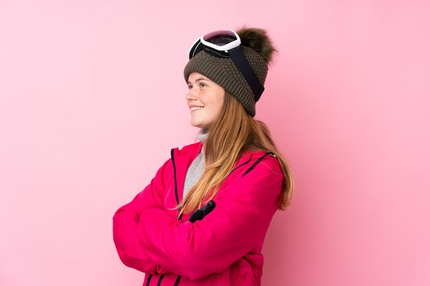 Foto oekraïens tienerskiërmeisje dat met snowboardglazen over geïsoleerd roze aan de kant kijkt