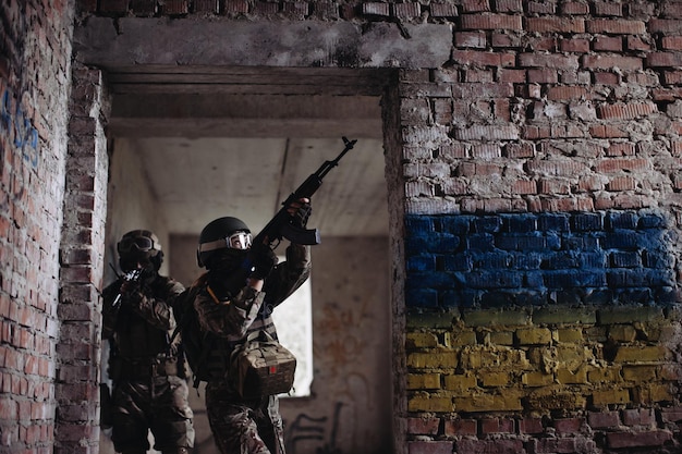 Oekraïense soldaten militair in de oorlog met een wapen in zijn handen De vlag van Oekraïne is geschilderd op een bakstenen muur Betrekkingen tussen Oekraïne en Rusland
