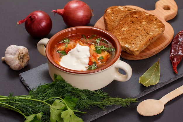 Oekraïense traditionele borsjt in porseleinen kom met roggebrood, peterselie, ui, knoflook en chilipeper op stenen bord. Bovenaanzicht.