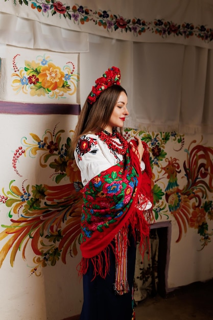 Foto oekraïense vrouw in traditionele etnische kleding en bloemen rode krans op achtergrond van versierd fornuis in hut oekraïense nationale geborduurde jurk oproep vyshyvanka bid voor oekraïne