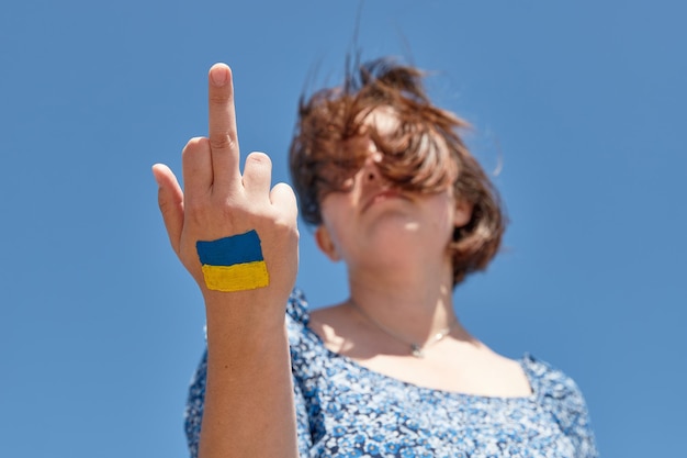 Oekraïense vrouw met een vlagsymbool op haar hand toont neukbord tegen de blauwe lucht, stop oorlog