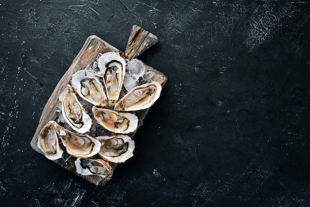 Oesters met ijs en citroen op zwarte stenen achtergrond Zeevruchten Bovenaanzicht Gratis kopieerruimte