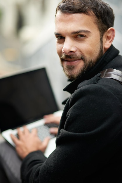 Of het nu voor werk of ontspanning is, ik ben de hele tijd verbonden Shot van een knappe jonge man die buiten een laptop gebruikt