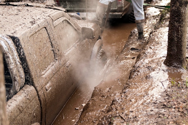 深い泥穴を通過するオフロード車。泥で満たされた汚れた車の詳細-洗車のコンセプト。車のホイール。汚れた車のホイールが林道に立っている