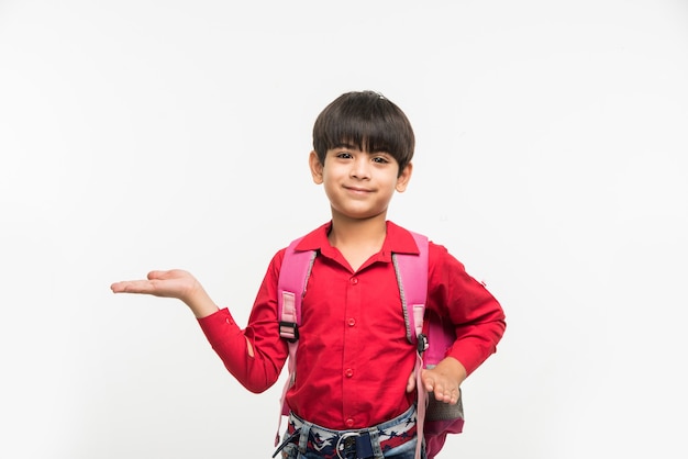 Off to School - Cute little Indian or asian boy in red shirt and denim jeans with school bag, standing isolated over white background