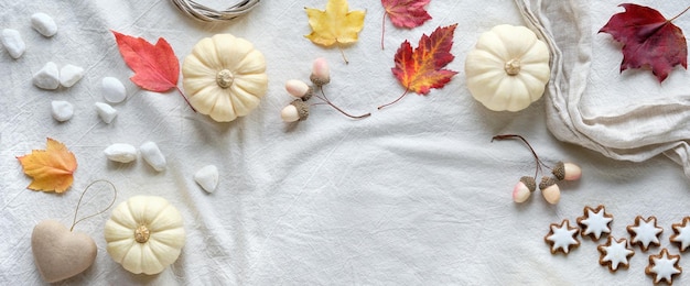 Off white natural Fall decorations with copy-space. Flat lay on white textile, place for text. Pumpkins, dry leaves and rowan berries, star cookies, dry leaves and craft paper heart.