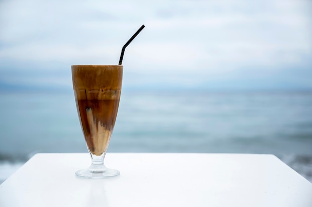 Фото Подача напитка с пеной и соломинкой на белом столе с морем