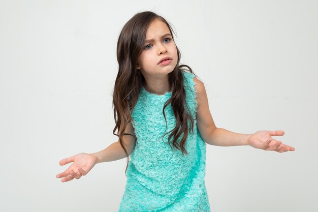 Offended girl in a blue dress doubts on a white studio wall