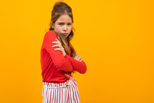 Offended girl crossed her arms on a yellow background with copy space.