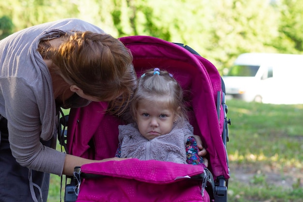 Offended little girl looking at camera and sitting in the pram and her mother looking at her