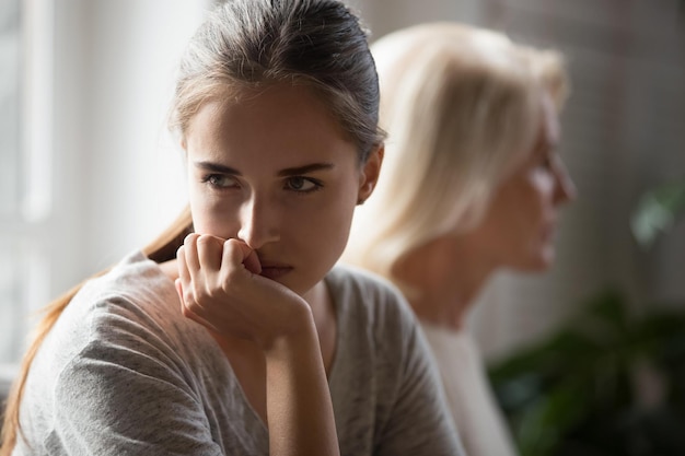 Offended millennial adult daughter and senior mother sit aside back to back avoid talking after fight hurt stubborn two generations of women ignore each other after conflict misunderstanding concept