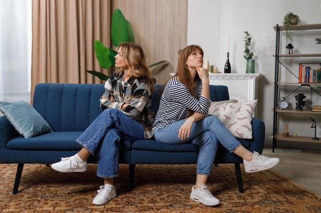 Offended mother and daughter sitting back to back on the sofa