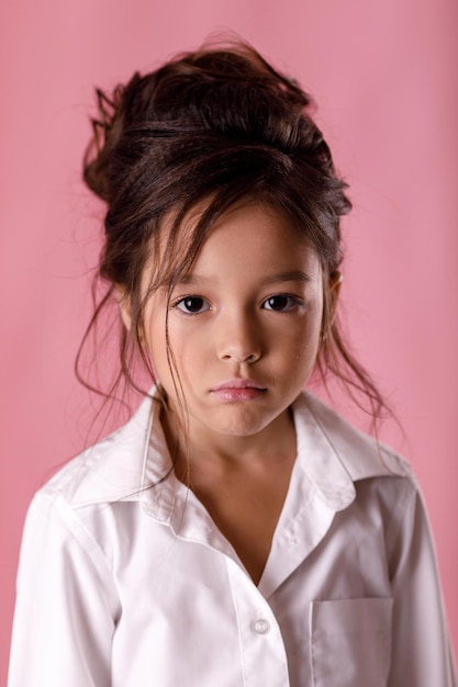 Photo offended sad bored little girl in white shirt on pink background. human emotions and facial expression