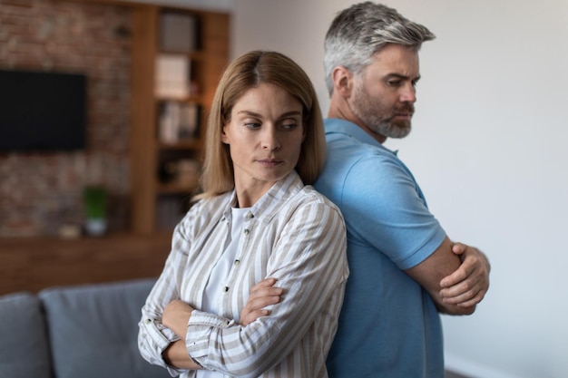 Offended upset adult european husband ignores wife man and woman stand back to back in room interior