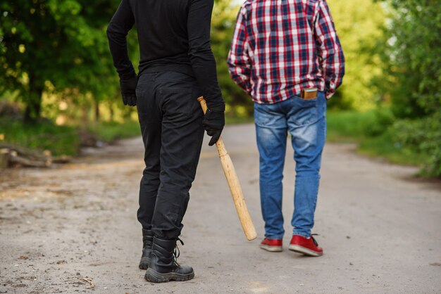 An offender in black clothes with a baseball bat in his hands\
attacks a man. pickpocketing on the street during daytime.