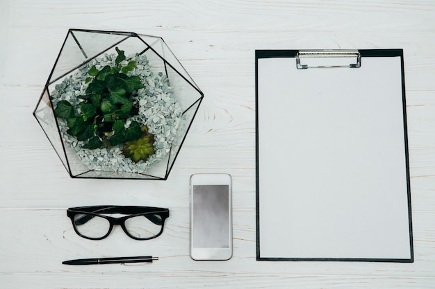 Office concept. Florarium vase, notepad, glasses and phone  on a white background.