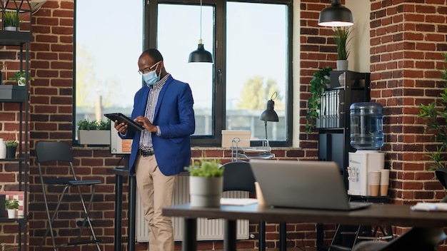 Office consultant waiting around in startup office using digital tablet, to find news about report. Pacing around workplace to analyze business statistics, feeling thoughtful and pensive.