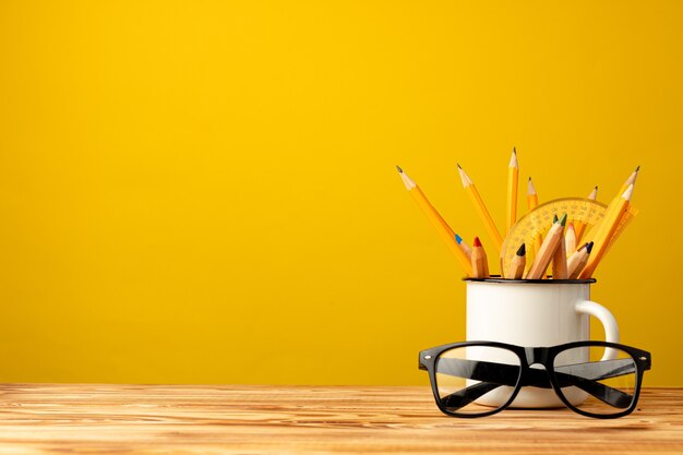 Office cup with pencils and stationery against yellow background front view