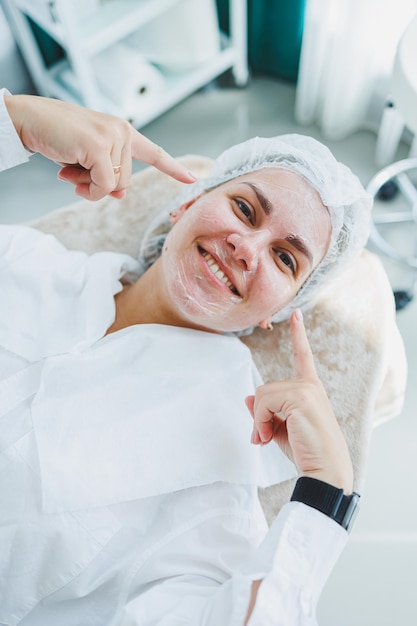 The office of a dermatologist or cosmetologist a woman lies with a mask on her face Facial skin care Closeup of a womans face with a white cosmetic mask