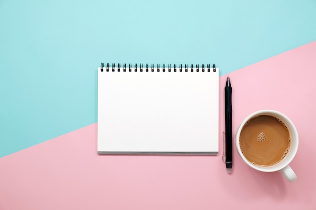 Office desk table with notebook, keyboard, pen, cup of coffee and flower. Top view with copy space.