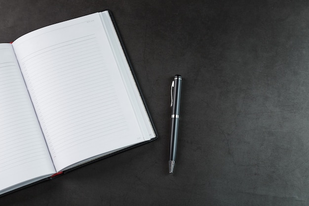 Office desk with black notepad and pen on black background. Top view with copy space. Business goals and objectives concept