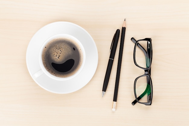 Office desk with coffee cup, supplies and glasses. View from above