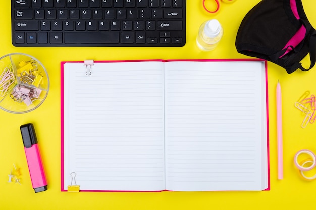 Office desk with computer and stationery, antiseptic and mask, yellow background