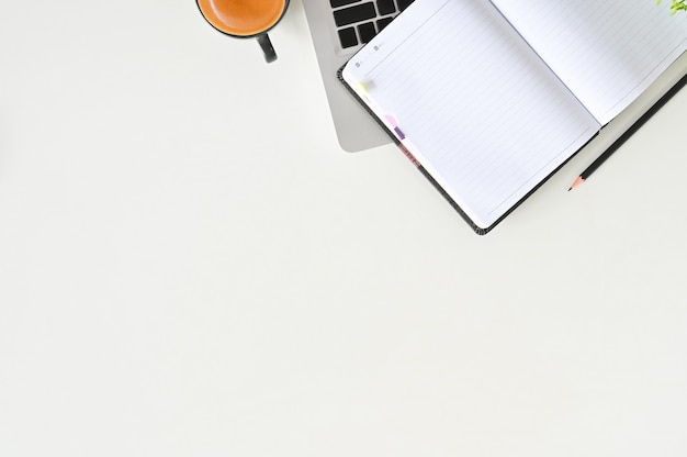 Office desk with laptop, coffee, notebook and pencil on white table top view.