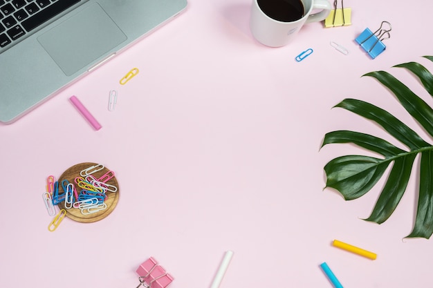 Office desk workspace with laptop and accessories on pink background. 