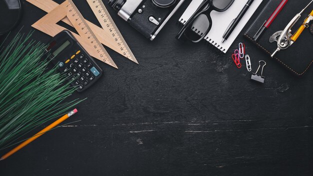 Office desktop Laptop camera calculator glasses ruler pen pencil On the black wooden surface Top view Free space for text