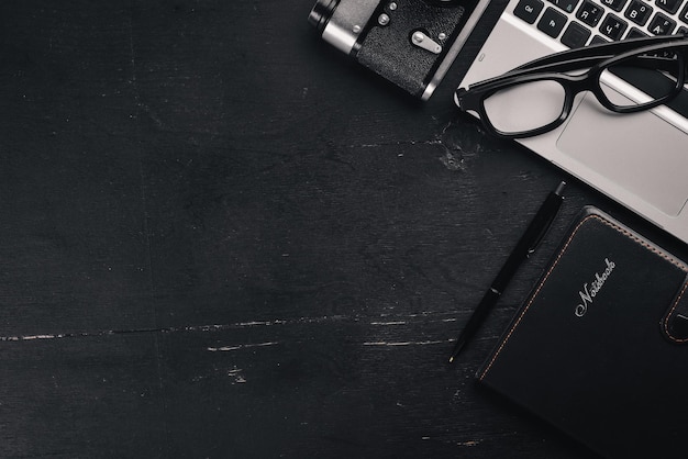 Офисный рабочий стол Ноутбук камера калькулятор очки линейка ручка карандаш на черной деревянной поверхности вид сверху свободное место для текста