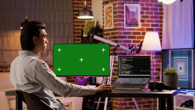 ホームデスクのコンピューターモニターでグリーンスクリーンを分析しているオフィスの従業員。分離されたモックアップ背景とコピースペース表示、PCプログラムで空白のクロマキーテンプレートを使用します。 。
