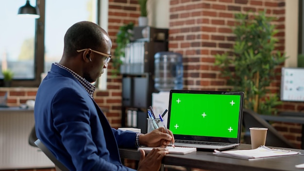 Office employee looking at laptop with greenscreen template, working in startup space. Sales consultant using isolated mockup background with chroma key display and blank copyspace.