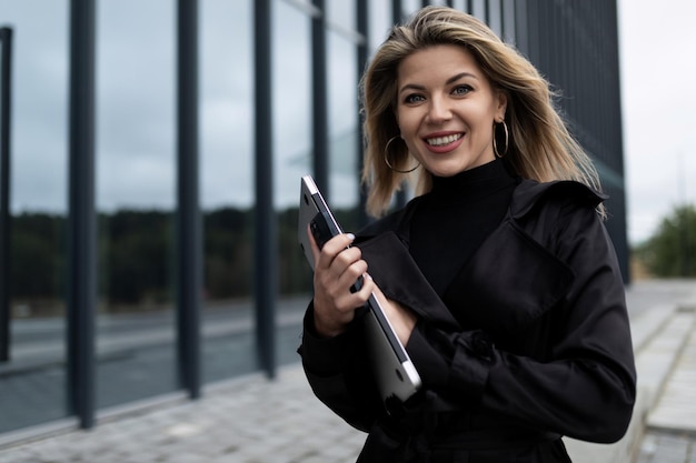 Office employee woman with a tablet in her hands hurries to work with a smile on her face against