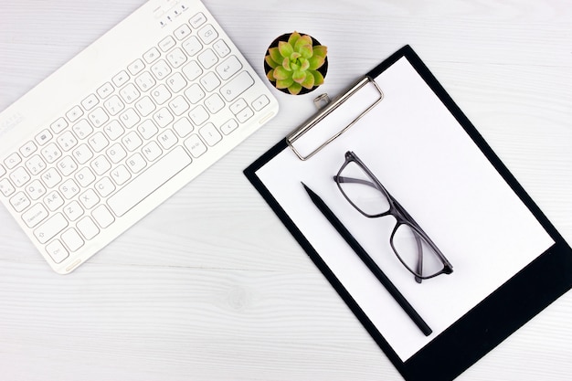 Office flatlay with white keyboard, reading glasses, pet and notebook