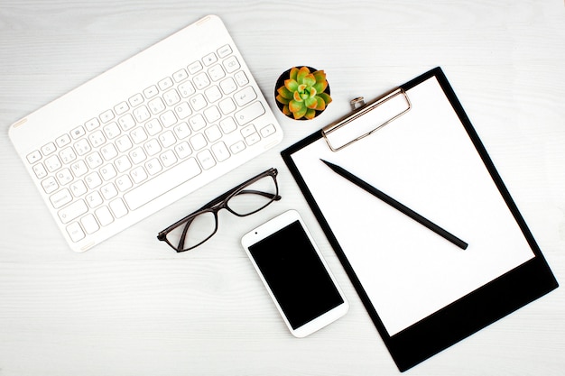 Office flatlay with white keyboard, reading glasses, pet and notebook.