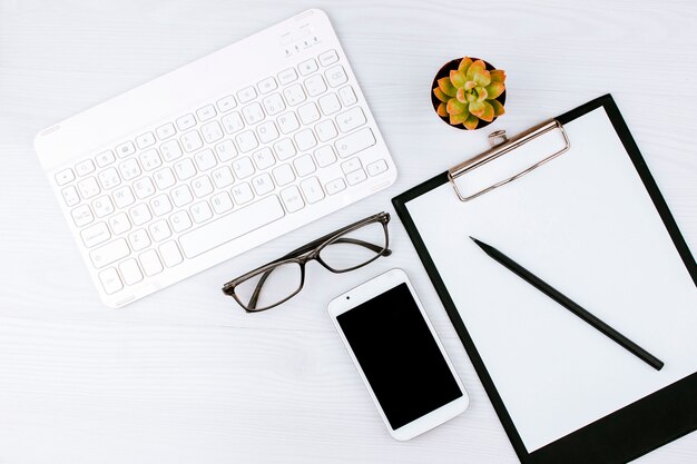 Office flatlay with white keyboard, reading glasses, pet and notebook